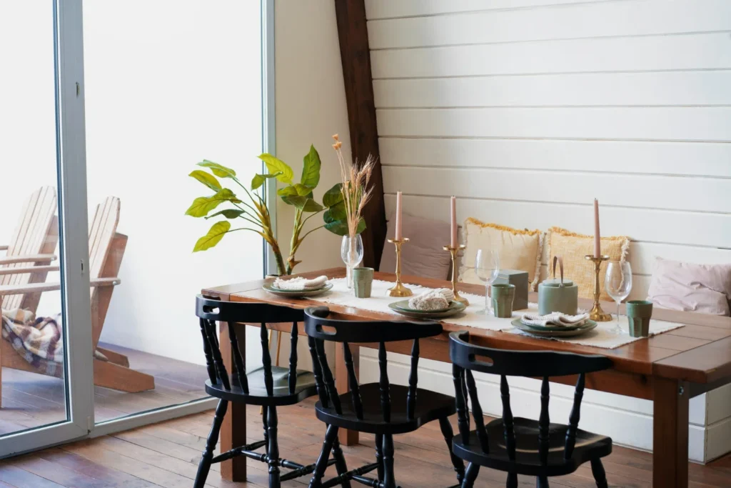 Móveis para cafeteria com mesa de madeira posta, cadeiras pretas e ambientação acolhedora